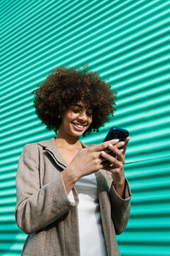 Smiling woman smartphone user texting against turquoise wall
