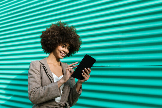 Smiling woman browsing tablet outdoors by a turquoise wall