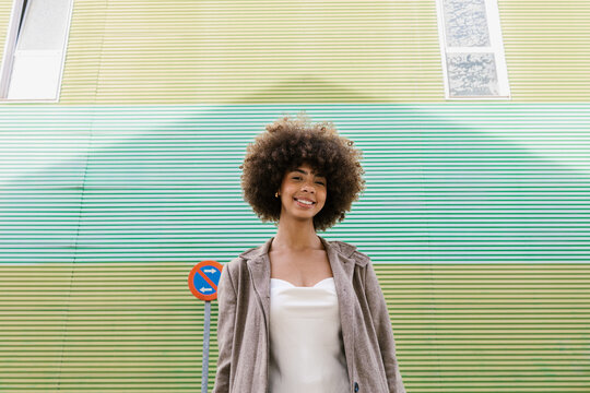 Smiling woman with afro hair standing by a striped wall outdoors