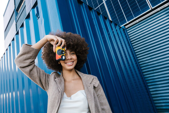 Cheerful photographer with afro hair taking picture outdoors