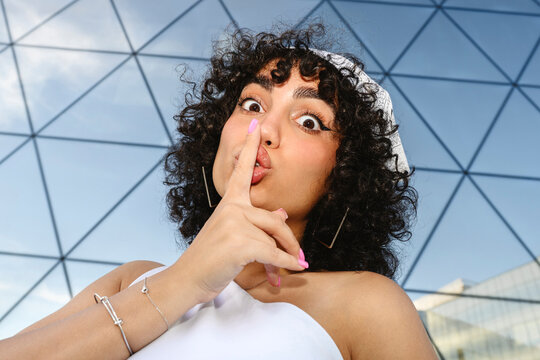 Playful woman gesturing silence outdoors by glass building