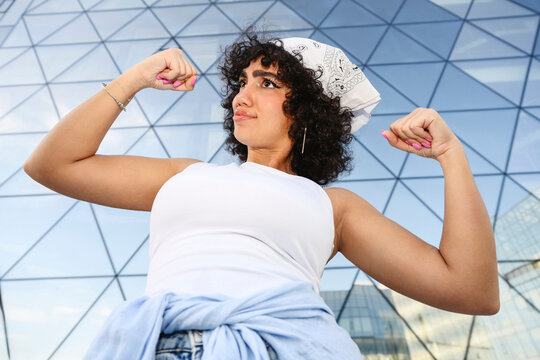 Confident iwoman flexing muscle outside modern glass building