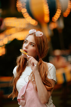 Fair visitor eating a lollipop at an illuminated amusement park