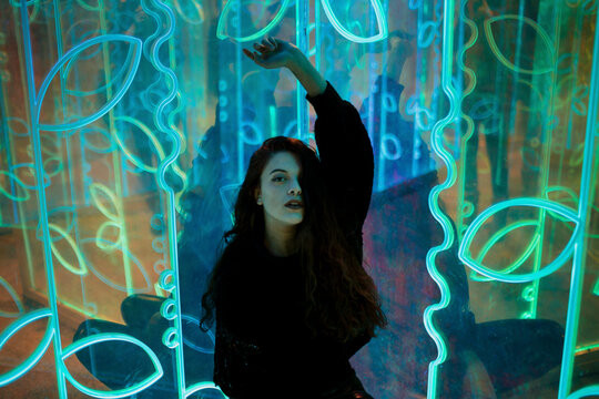 Dancer looking at camera behind a glowing neon installation