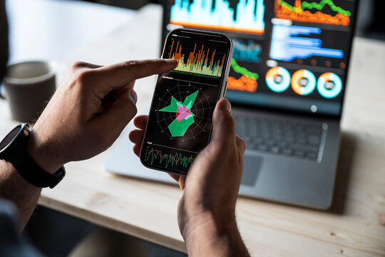 Hands holding smartphone with financial data at the office desk