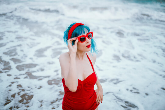 Model with blue hair in red swimsuit standing in ocean