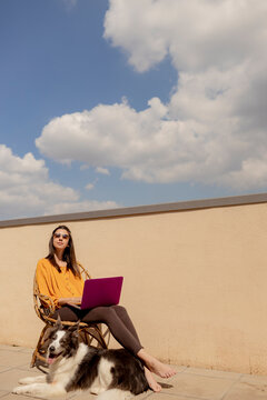 Freelancer woman telecommuting on sunny balcony with her dog