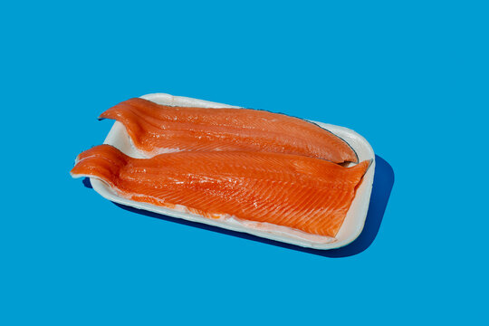 Fresh raw trout fillets in white foam tray on blue background