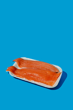 Raw fresh trout fillet on white disposable tray with blue background