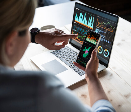 Analyst reviewing financial data on laptop and phone in office