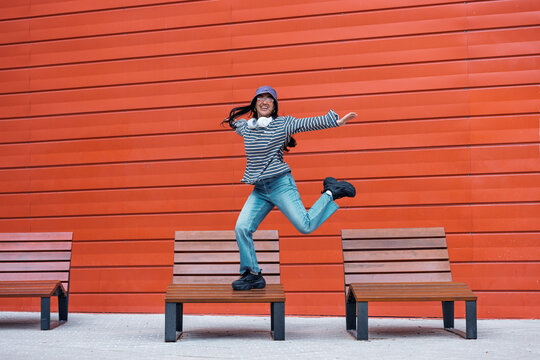 Smiling woman jumps over wooden benches on the street