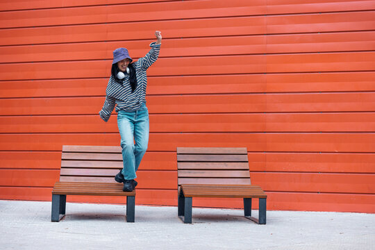 Woman dancing playfully on an outdoor bench against an orange wall