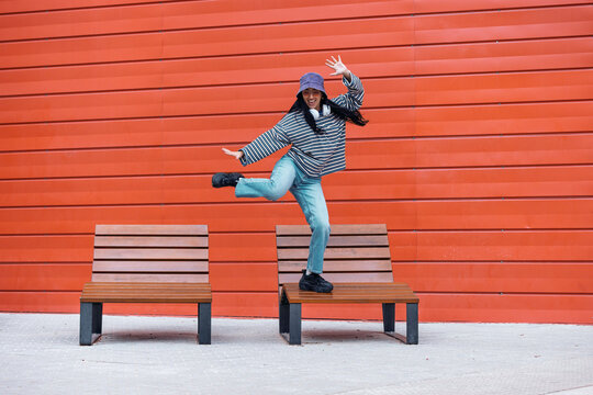 Female dancer balancing on a wooden bench against an orange wall outdoors