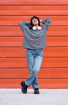 Relaxed woman in bucket hat leaning against orange wall outdoors