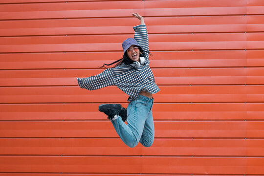 Woman jumping and dancing with energy outdoors against an orange wall