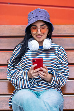 Smiling woman sitting on street bench outdoors using smartphone
