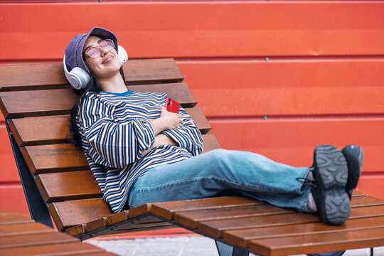 Woman relaxing on outdoor bench listening music on smartphone