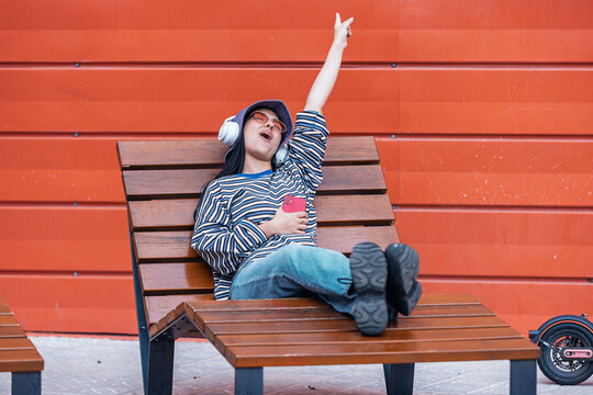 Relaxed woman sitting on street bench listening to music and singing