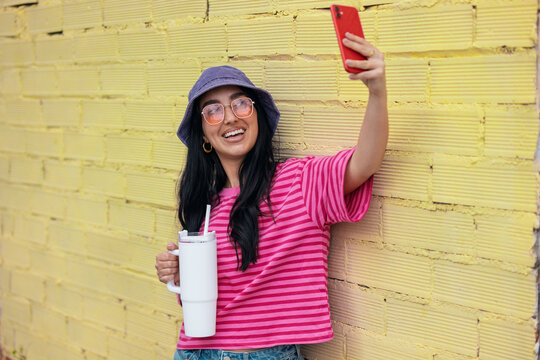 Smiling influencer taking a relaxed selfie against a yellow wall