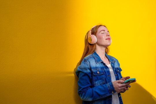 Redhead in denim jacket listening to music on smartphone