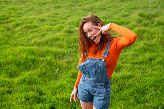 Smiling with red hair making victory sign in a grassy field