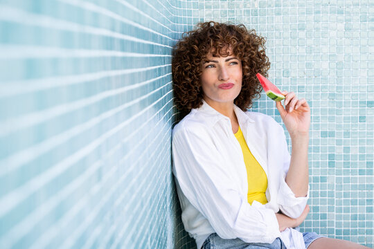 Model holding a watermelon slice in an empty tiled pool in summer