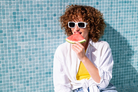 Woman eating watermelon by an empty pool in summer