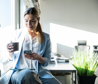 Smiling employee reading smartphone message during office break