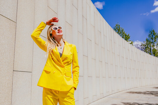 Happy freelancer in yellow suit shielding eyes from sun outdoors
