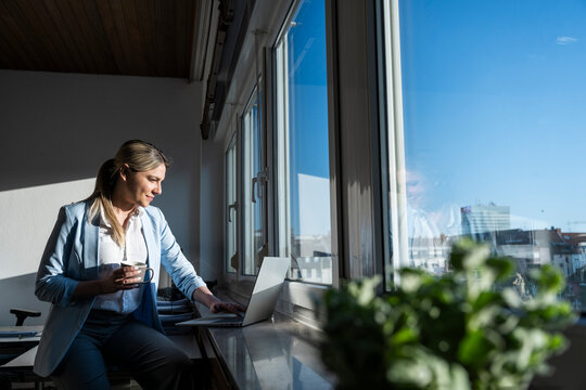 Smiling businesswoman working on notebook by office window