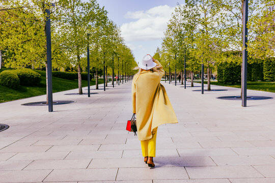 Freelancer walking in a modern park wearing a yellow coat and hat