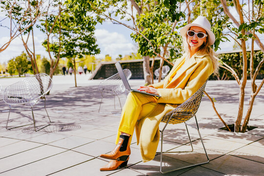 Smiling freelancer in yellow coat using laptop outdoors