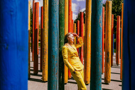 Happy businesswoman in yellow suit leaning on pillar in park