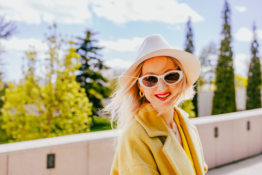Happy freelancer with hat and sunglasses smiling in sunny park