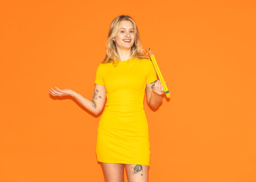 Smiling in a yellow dress and holding a paper pencil