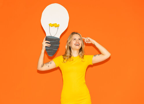 Model in yellow dress holds paper light bulb pointing to head