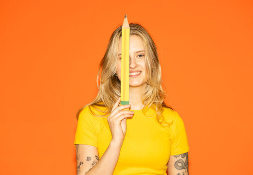 Smiling student holding a large pencil for brainstorming indoors