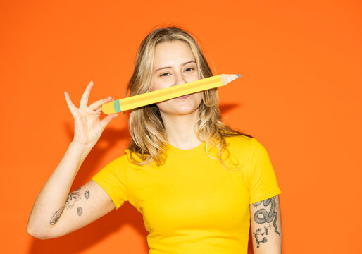 Designer holding paper pencil like a mustache on orange background