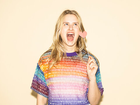 Woman holding a paper heart prop and wearing a multicolored sweater