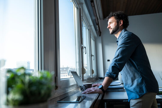 Business person standing at office window thinking with notebook