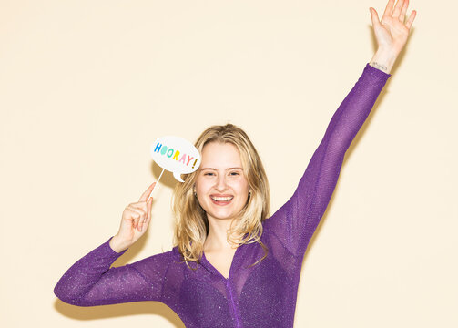 Smiling woman cheering with a hooray sign in purple full body suit