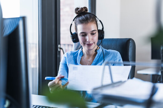Smiling businesswoman reading document with headset at office desk