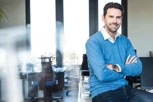 Smiling businessman sitting on desk in modern office