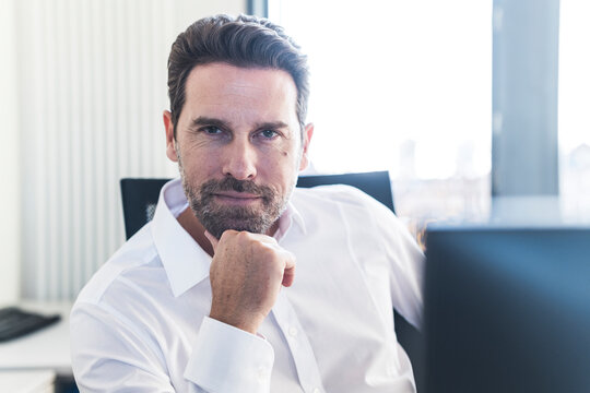 Confident businessman thinking at desk in office looking at camera