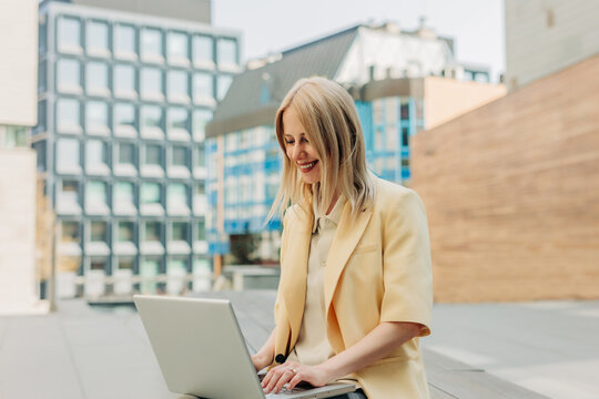 Smiling businesswoman working on laptop outdoors in modern city