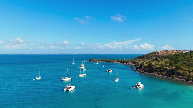 Drone view of sailboats and catamarans anchored in a calm tropical bay near Friar's Bay Beach on Saint Martin island. The turquoise ocean waters surround the lush green coastline Caribbean destination