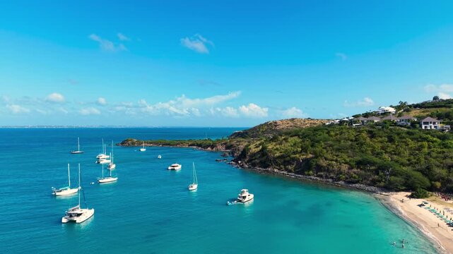 Drone view of sailboats and catamarans anchored in a calm tropical bay near Friar's Bay Beach on Saint Martin island. The turquoise ocean waters surround the lush green coastline Caribbean destination