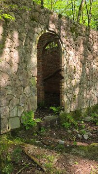 Ancient stone and brick wall structure featuring an arched doorway stands partially covered by nature, symbolizing decay, abandonment, and the passage of time