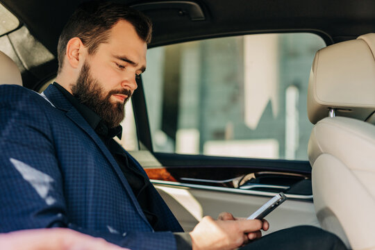 Businessman in suit using smartphone in back seat of car