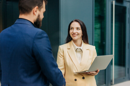 Smiling boss and job seeker with laptop shaking hands outdoors